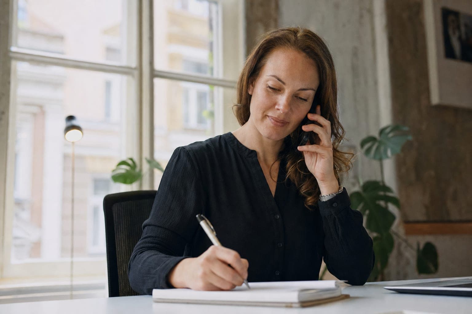 Recruiterin im Telefonat mit Notizblock am Schreibtisch